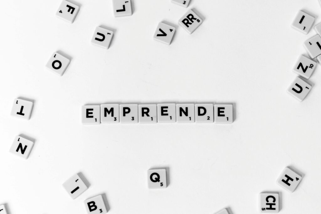 Scrabble tiles laid out to spell 'EMPRENDE' creatively on white background.